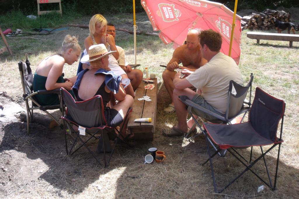 Een groepje Ouwe Bollen zit in kampeerstelen te kaarten op een bankje in de schaduw van een parasol.