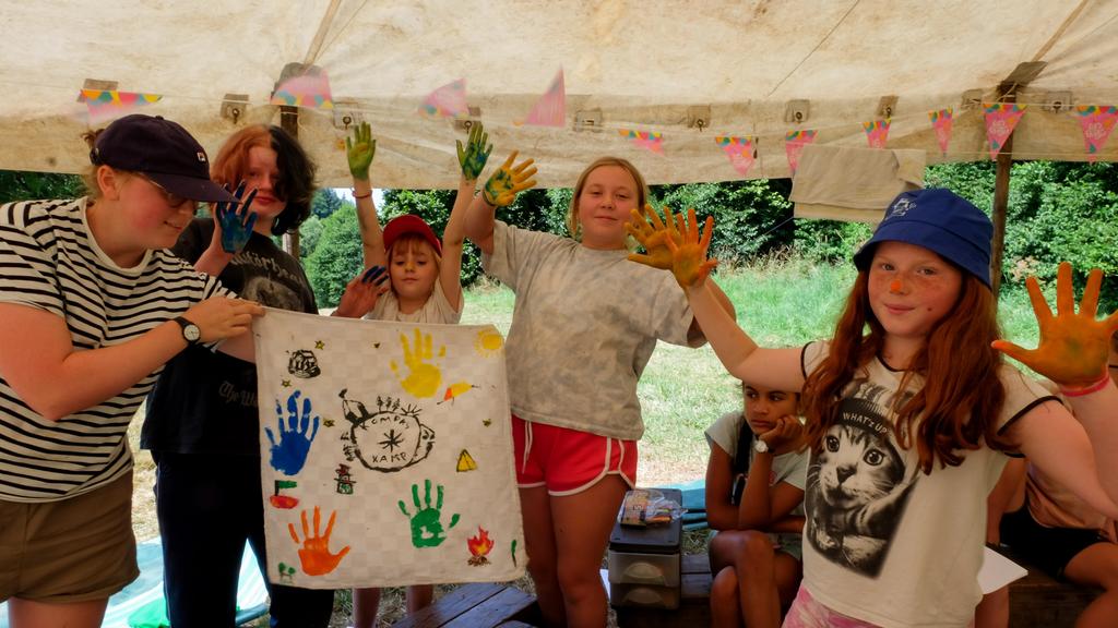 Kinderen tonen hun handen vol vingerverf waarmee ze net een vlag hebben gemaakt in Kompasstijl.